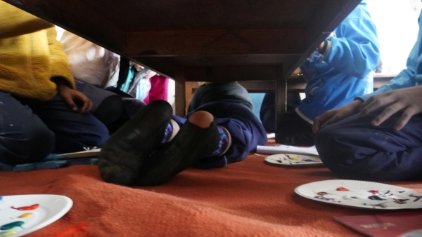 机の下にもぐって描いている男の子。靴下が破けていますね