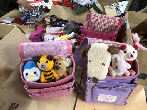 ぬいぐるみやおもちゃの仕分け風景です。大きなテーブルで、みんなで輪になって作業しています。